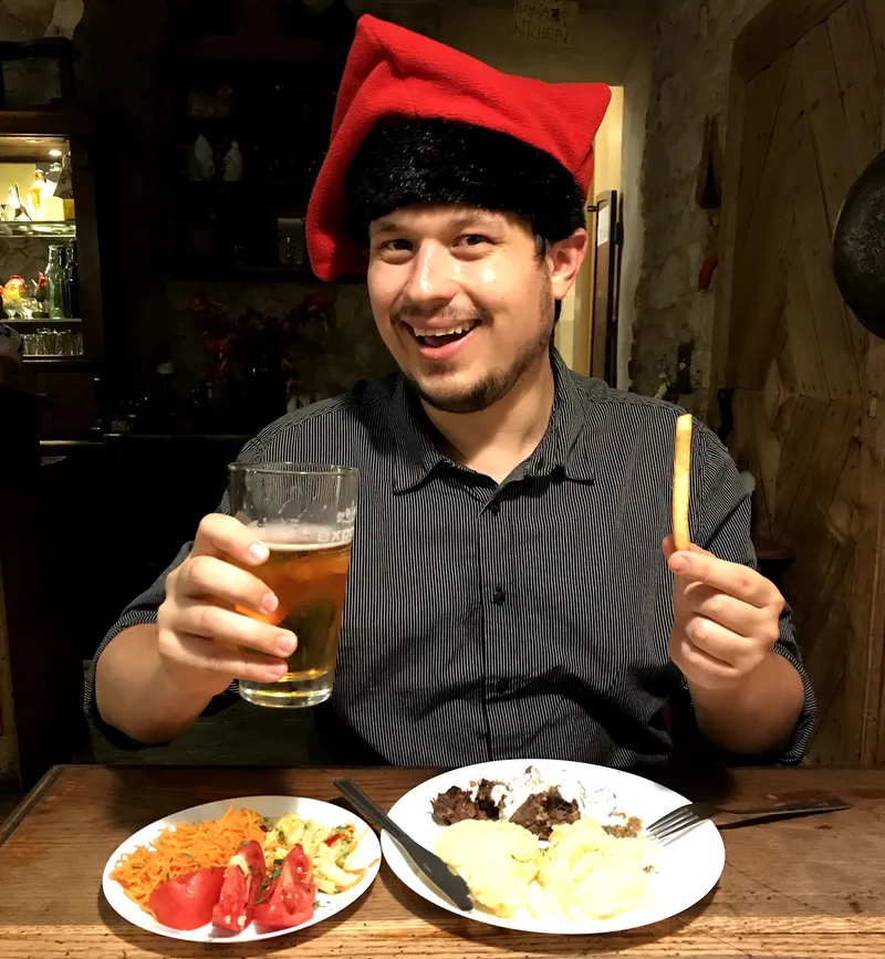 Konrad in a red jester cap with a beer and a plate of Polish food