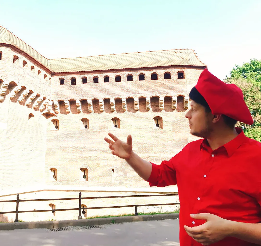 Konrad in a red jester cap pointing at the brick wall of the Barbican