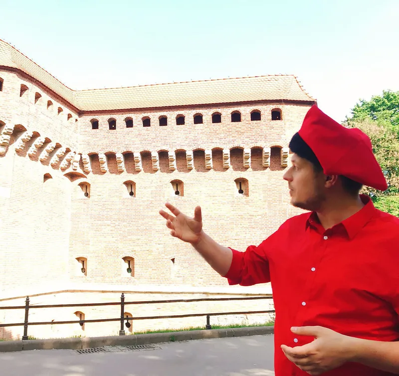 Konrad in a red jester cap pointing at the brick wall of the Barbican
